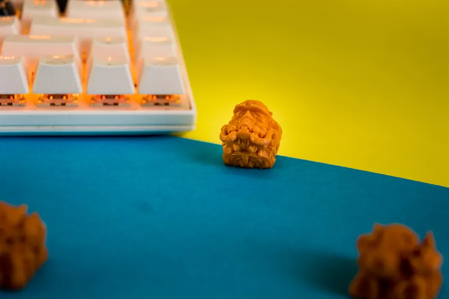 Meltspawn keycap beside a white keyboard on a yellow and teal backdrop